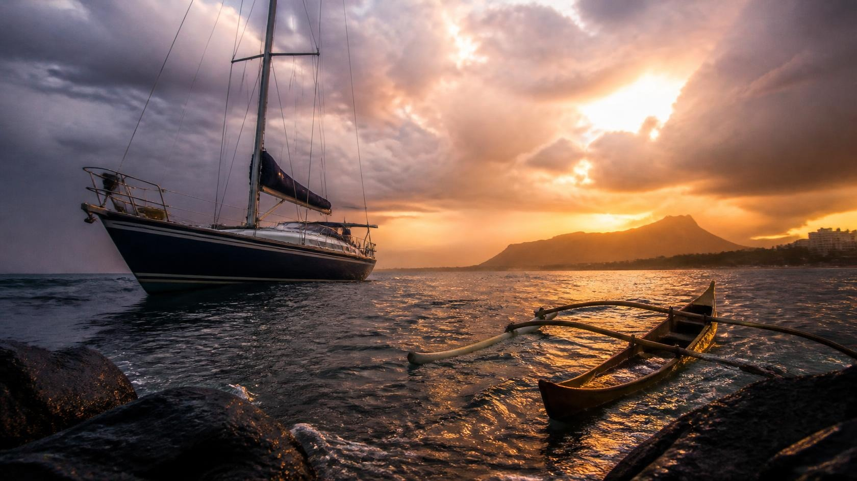 A sailing yacht rides high on the tide in a Hawaii harbor after a storm while a small outrigger canoe sits low and leaking beside it, golden sunset light breaking through clouds over Diamond Head.